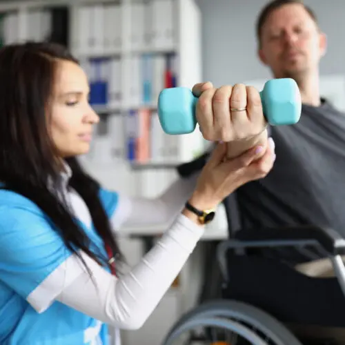 nurse assists man in wheelchair with rehabilitation exercises using a small dumbbell