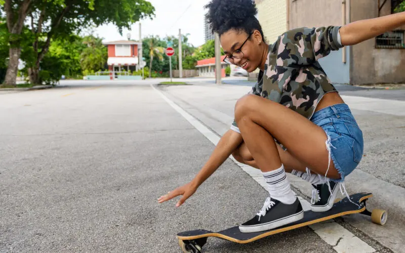 young woman riding low on a longboard on a city road