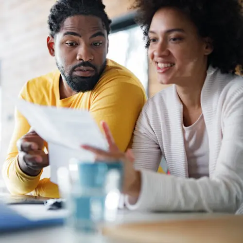 a couple sitting at their kitchen counter with their laptop looking over a pice of paper