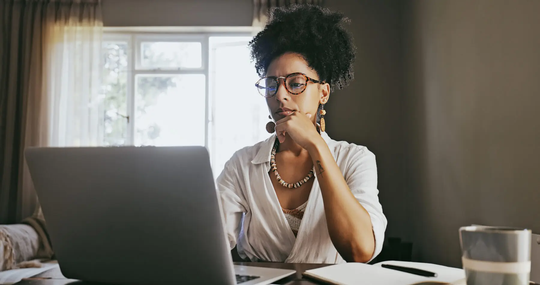woman sitting at desk looking thoughtfully at her laptop screen