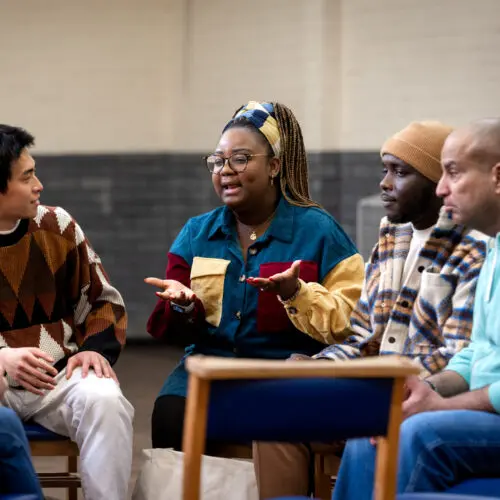 a group of people sitting in a circle focused on a woman speaking to her fellow community members