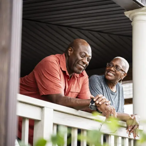 a couple smiles as they lean over the railing on their front porch
