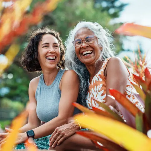 an older mother and daughter sitting side by side and laughing