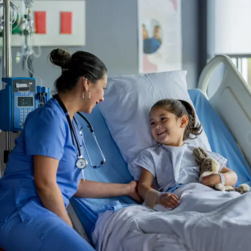 nurse sits beside hospital bed with a smiling child