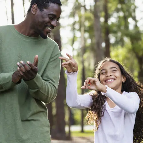 a father, young daughter, and mother walk through a park