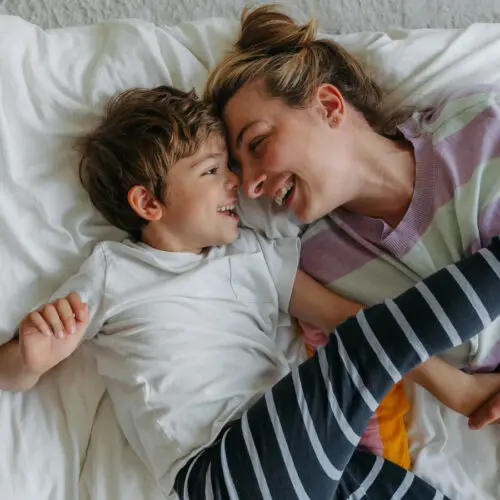 mother and son touching foreheads and smiling while laying on a bed