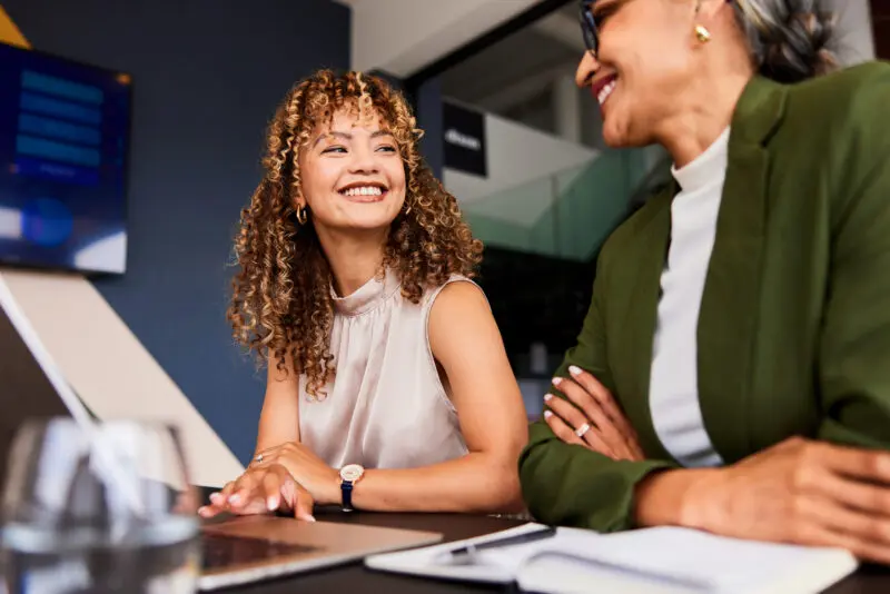Cheerful young businesswoman smiling confidently towards female colleague at work