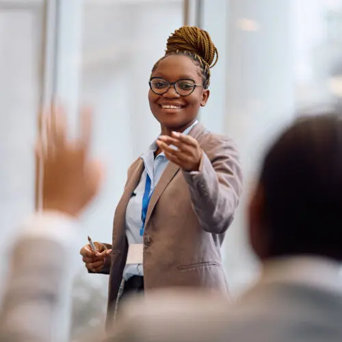 business woman standing as she gives a presentation and points to someone with their hand raised