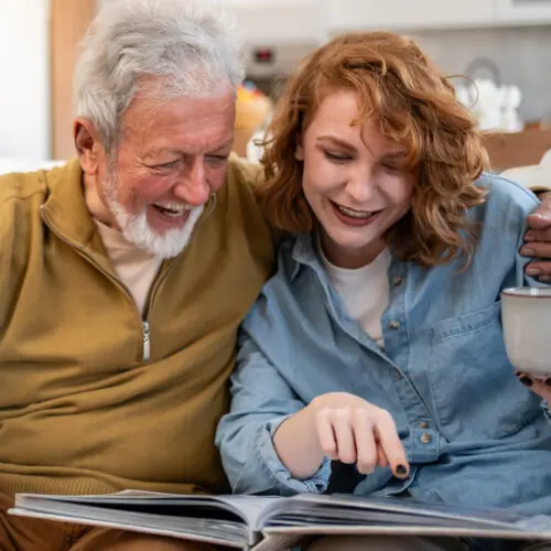 older couple sitting and smiling as they look through a photo album