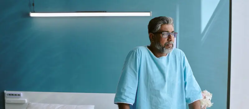 man in hospital room standing with walker gazing out a window