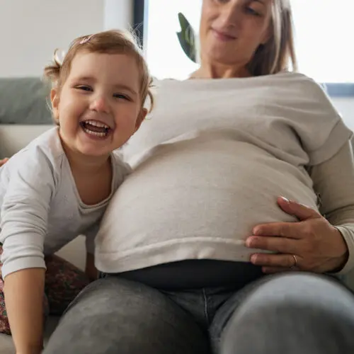 young child smiling at camera next to her pregnant mother