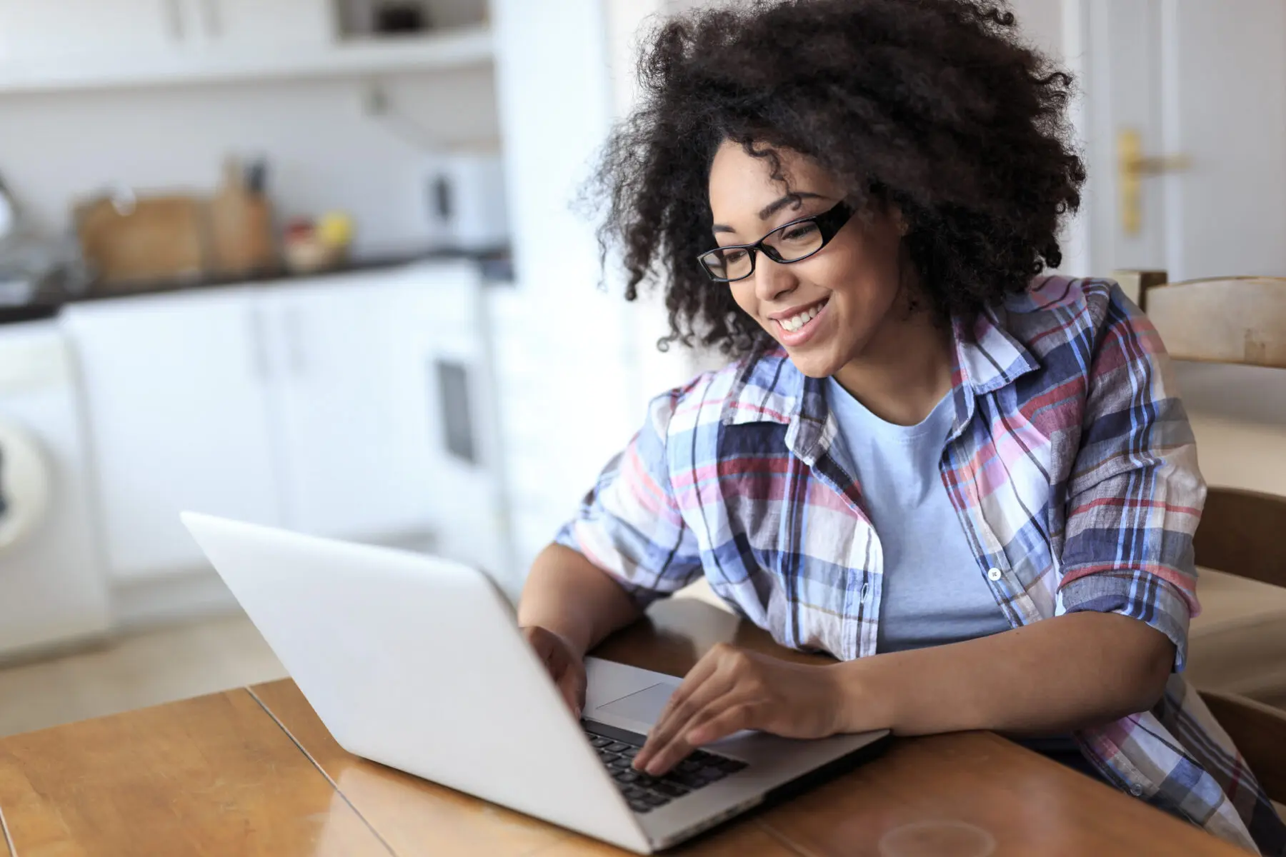 woman sitting at table in her home, smiling as she types on her laptop